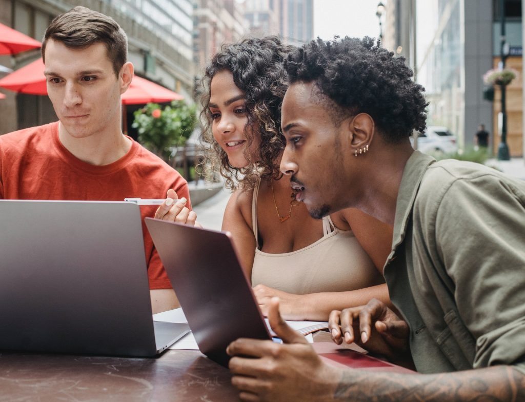 Three people looking pleasantly amused at a laptop screen outdoors