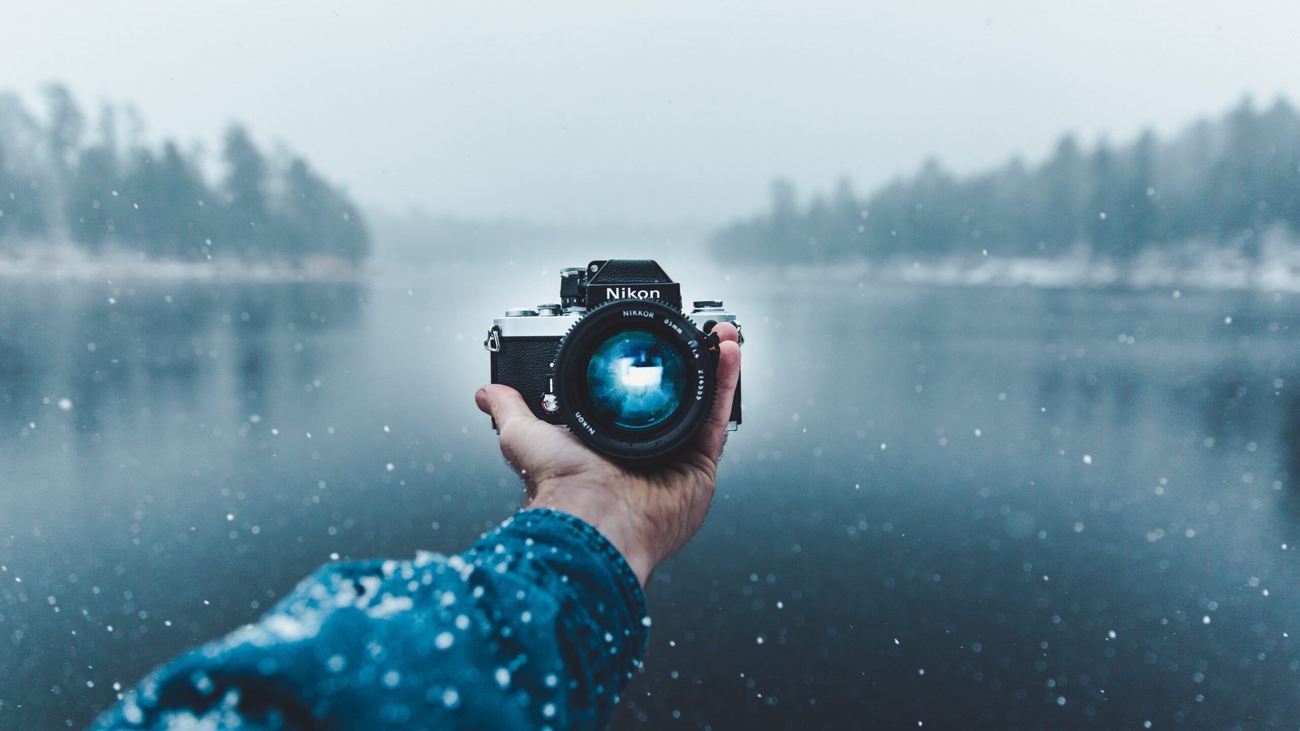 A person holds out a camera over a lake.