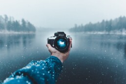 A person holds out a camera over a lake.