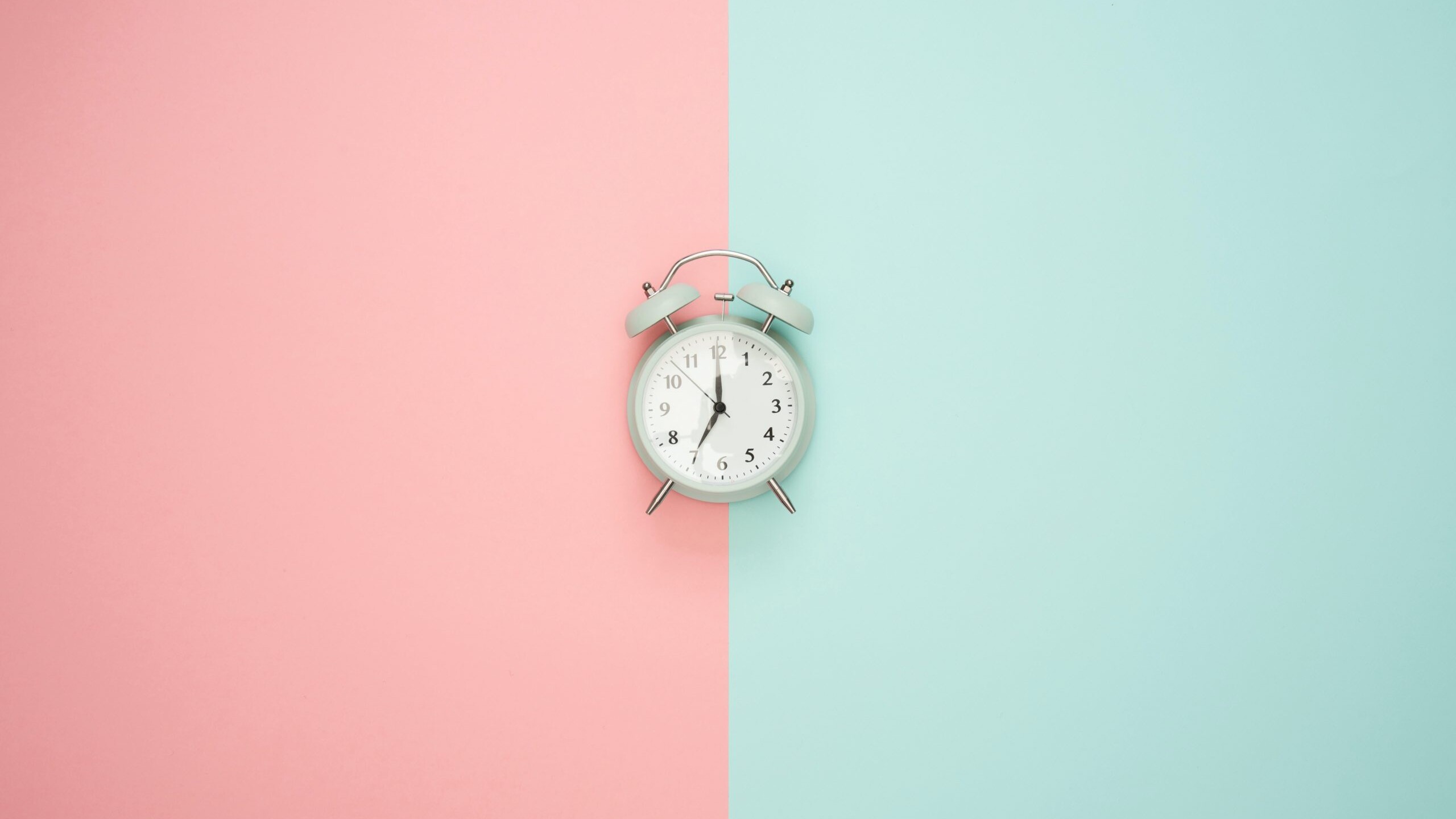 An alarm clock sits on a pink and teal backdrop.