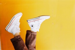 A person's shoes dangle against a yellow backdrop