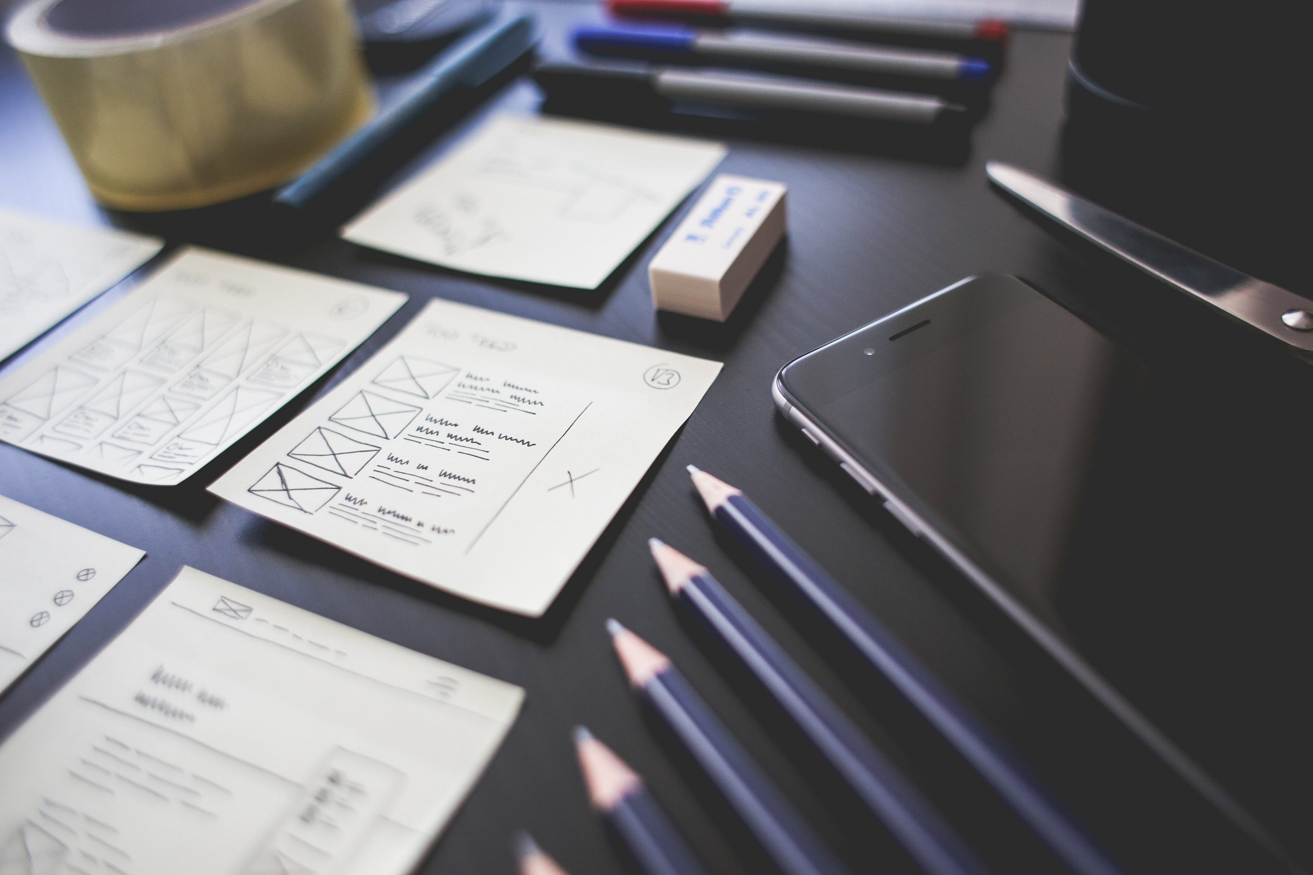 A desk with wireframe sketches and pencils sit on top