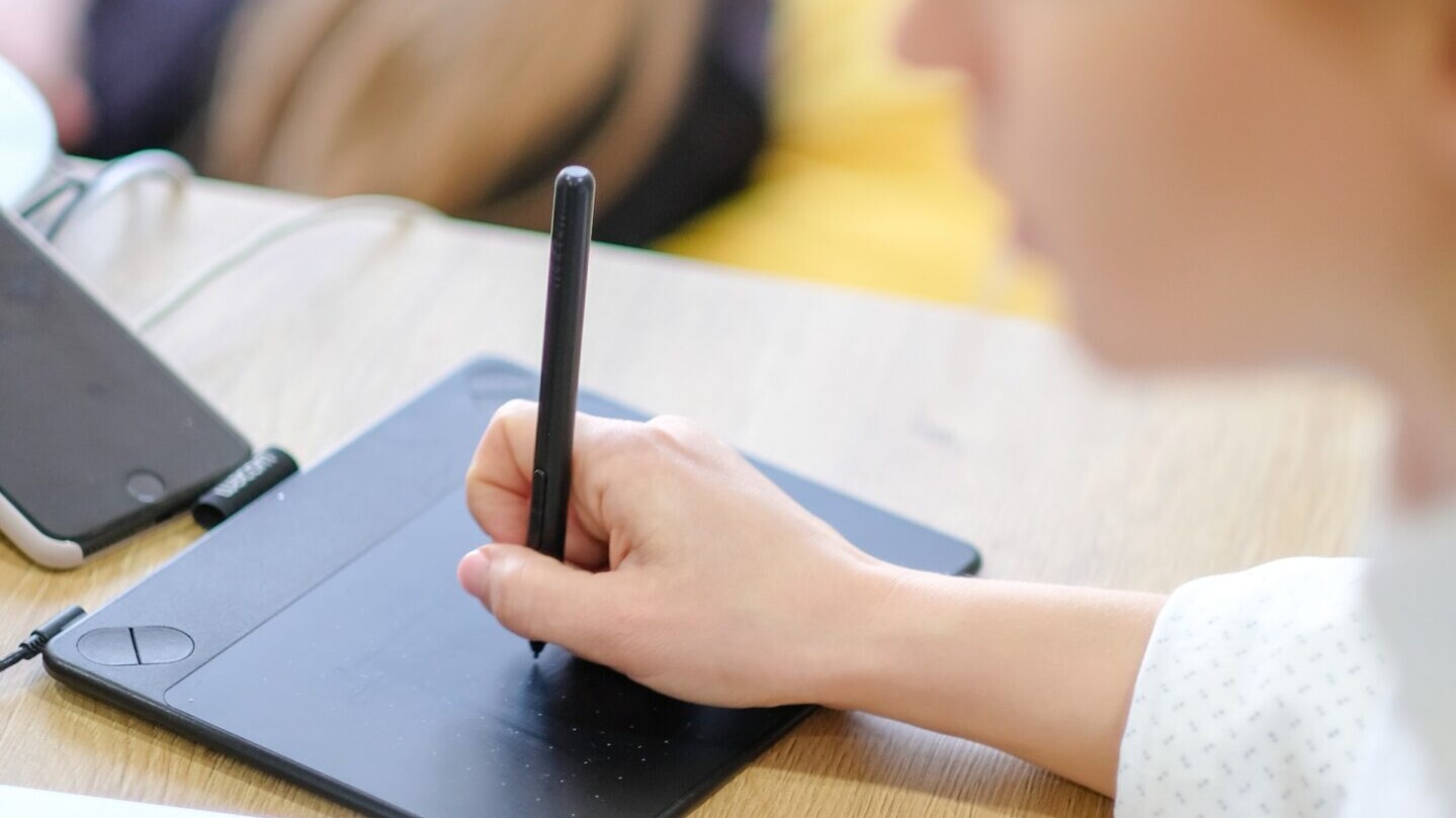 A person uses a stylus and pad next to their laptop, to develop graphic design.