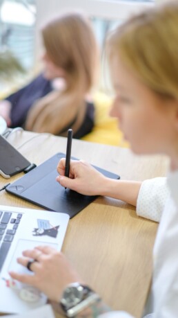 A person uses a stylus and pad next to their laptop, to develop graphic design.