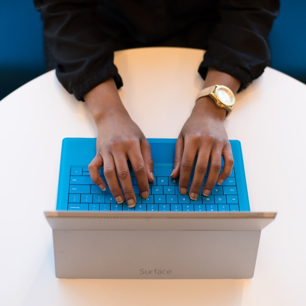A person typing on laptop with a blue keyboard.