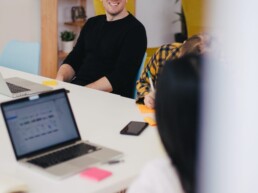Two designers sit on a desk and chat. One smiles, the other is out of focus.