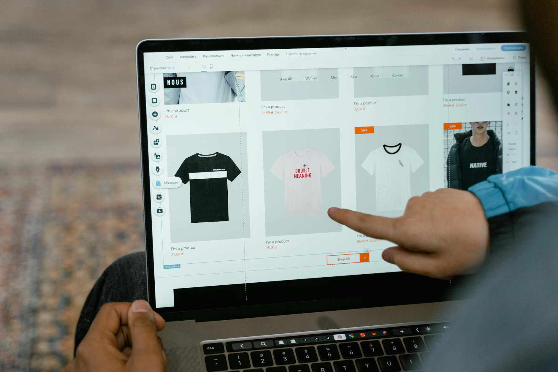 Person pointing at clothing items displayed on a laptop screen during online shop design.